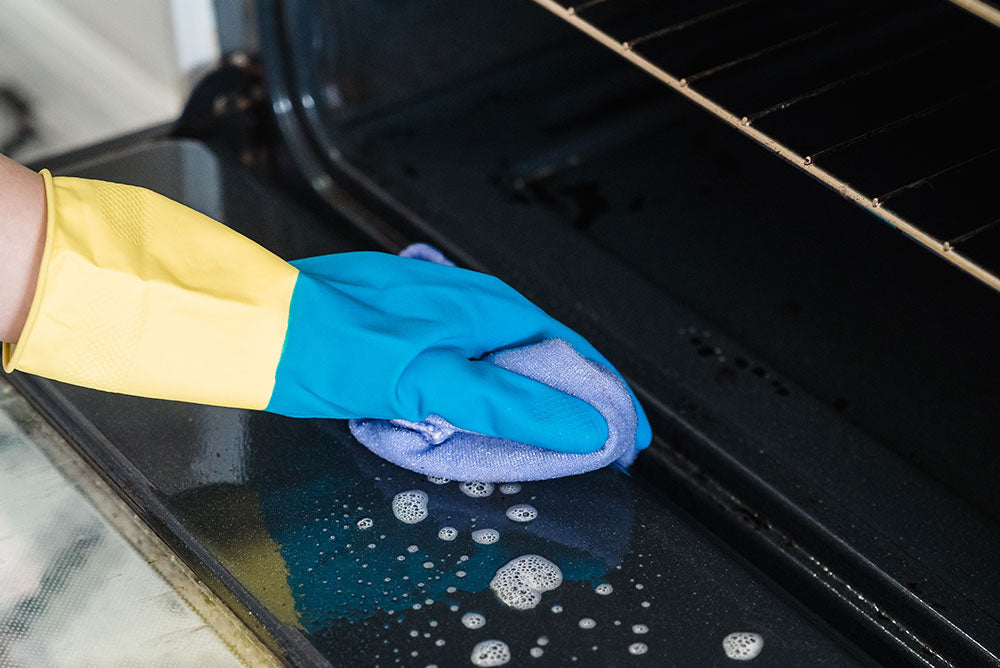 Person cleaning an oven door with baking soda and vinegar using a microfiber cloth